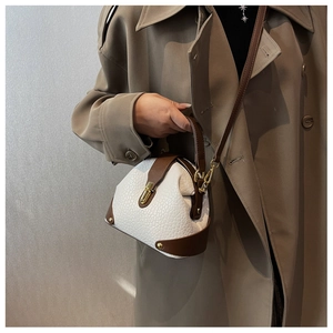 Detailed close-up of textured leather shell bag with gold hardware and contrast stitching