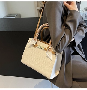 Detail of stone embossed cream handbag with silk scarf handle and golden lock clasp