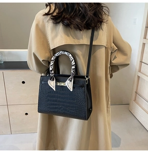 Detail of black crocodile pattern faux leather handbag with silk scarf on handle