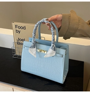 Close-up of light blue crocodile pattern handbag with elegant silk scarf on handle