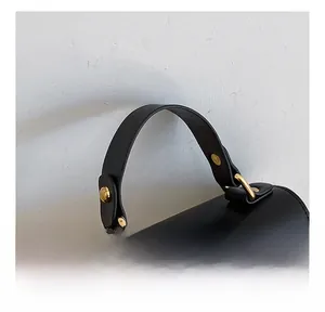 Detail of black leather handle with gold studs and woven texture on a minimalist bag