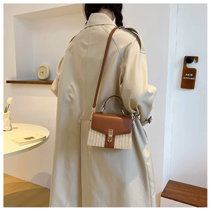 Close-up of woven crossbody bag featuring brown leather flap and polished metal lock