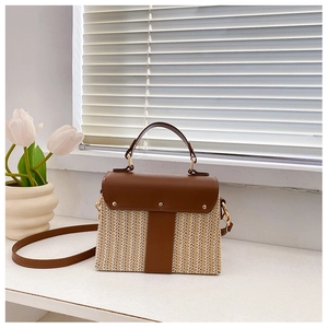 Detail of woven straw shoulder bag featuring brown leather flap and gold rivet accents