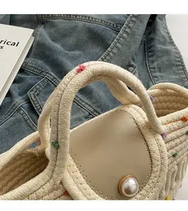 Gros plan d'un sac en paille tissée avec fermoir perle et pompons colorés sur denim