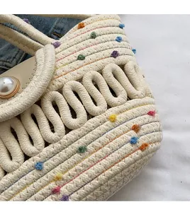 Détail du sac tressé avec pompons colorés et boucle perle sur un fond en denim bleu