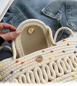 Détail d'un sac à main tissé beige avec pompons colorés et fermoir magnétique doré