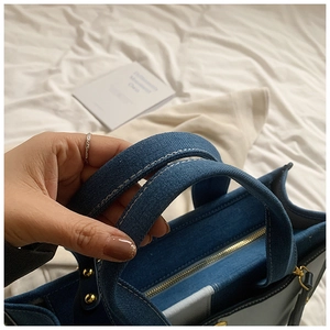 Gros plan détaillé du sac cabas en jean bleu avec coutures blanches et rivets dorés