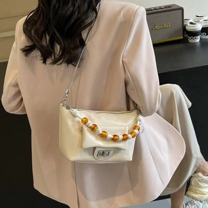 Detail of cream leather shoulder bag featuring amber beaded chain and metal turn-lock