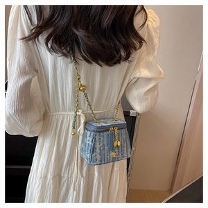 Detail of blue tweed mini crossbody bag with gold chain and floral charm on model