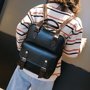 Detail of a large capacity black faux leather backpack with brown contrast straps on a model