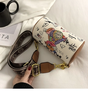 Détail du sac cylindre graffiti avec bandoulière à motifs et boucles dorées