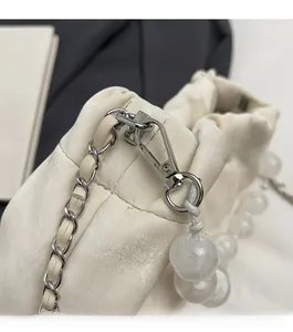 Detail of silver metallic clasp and elegant pearl beads on a white pleated handbag