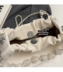 Detail of cream pleated crossbody bag showing magnetic closure and faux pearl accents