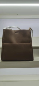 Detail of a brown lychee-textured leather tote bag with a front pocket on a white shelf