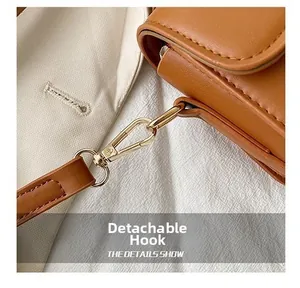 Detail of a brown leather bag showing golden detachable hooks and fine shoulder strap stitching