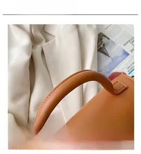 Detail of a brown leather shoulder bag featuring a thick reinforced cylindrical handle