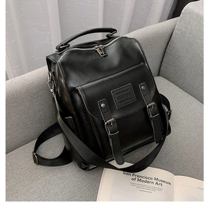 Versatile black PU leather backpack with silver zippers on a gray sofa background