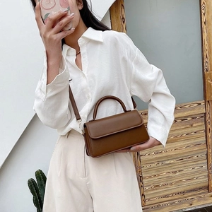 Brown matte leather crossbody bag with flap and metal buckle shown on a female model