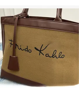 Close-up of khaki canvas tote bag featuring brown leather trim and Frida Kahlo script