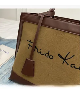 Close-up of khaki canvas tote bag with brown leather trim and cursive lettering print