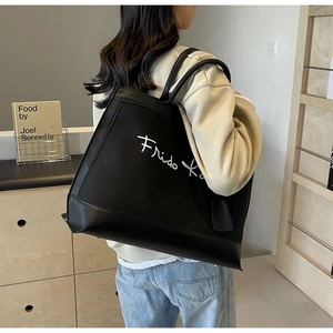 Detail of black canvas tote bag with Frida Kahlo script and leather handle contrast