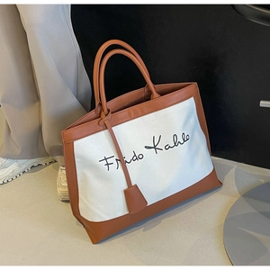 Detail view of canvas tote bag featuring brown leather trim and Frida Kahlo signature logo
