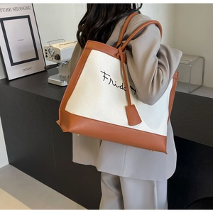 Detail of canvas tote bag featuring brown leather trim and Friday embroidery on shoulder