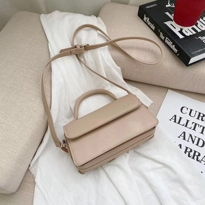 Minimalist beige crossbody bag with top handle and gold hardware on white cloth