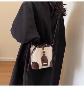 Detail of canvas bucket bag with brown leather trim and metal clasp on shoulder