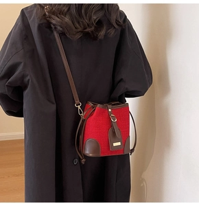 Close-up of red woven bucket bag with brown leather trim on dark wool coat background