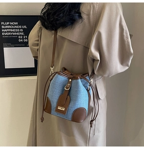 Detail of blue woven bucket bag featuring brown leather trim and drawstring closure