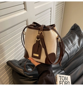 Detail of beige woven bucket bag with brown leather trim and drawstring closure