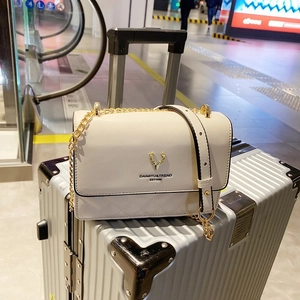 Detail of cream quilted crossbody bag with gold deer logo on a silver suitcase