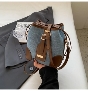 Detail of blue canvas bucket bag with brown leather trim and golden hardware