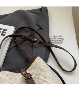 Detail of adjustable leather strap with gold buckle on a beige woven bucket handbag