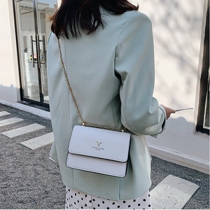 Minimalist white flap chain bag with golden deer logo worn by a model in outdoor setting