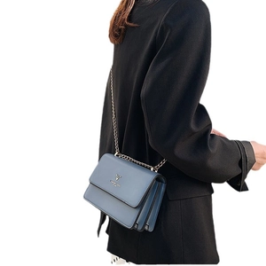 Minimalist blue-gray crossbody bag with gold chain strap worn over a black blazer
