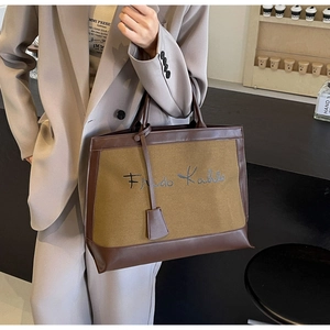 Canvas tote bag with Frida Kahlo signature and brown leather trim shown in street style