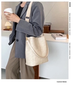 Detail der beigen Beuteltasche mit Krokodilmuster, breitem Stoffgurt und goldener Hardware
