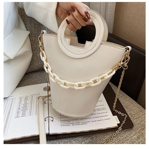 Minimalist beige bucket bag with circular cutout handle and plastic chain strap