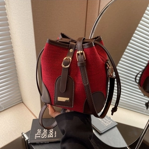 Red fabric drawstring bucket bag with brown leather trim and golden metal hardware