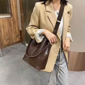 Dunkelbraune Beuteltasche mit Krokodilprägung und breitem Textilgurt am Model
