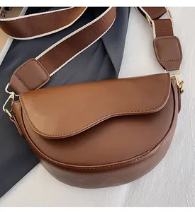Close-up of brown faux leather saddle bag with striped wide shoulder strap and gold hardware