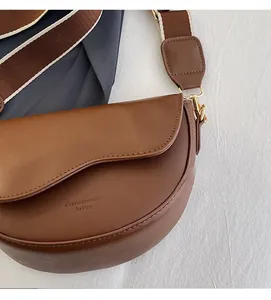 Close-up of brown saddle bag featuring wide striped strap and gold hardware details