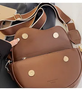 Detailed close-up of brown saddle bag with magnetic clasp and wide canvas strap