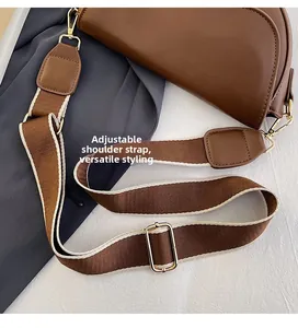 Detail of adjustable wide fabric strap with gold metal buckle on a brown saddle bag