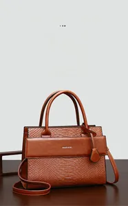 Detail of caramel brown crocodile embossed tote with silver logo on wooden surface