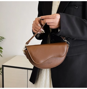 Detailed view of brown leather saddle bag with wavy flap and long shoulder strap