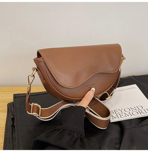 Detail of a brown leather saddle bag with a dual-color striped wide fabric strap