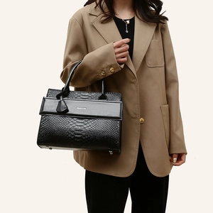 Elegant black shoulder bag with crocodile texture and silver logo held by female model
